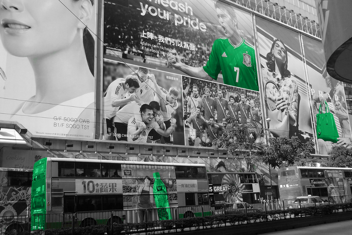 Street scene in Hong Kong featuring bold billboard ads, buses, and a pop of green highlighting brands, reflecting the commercial and creative energy of the city.