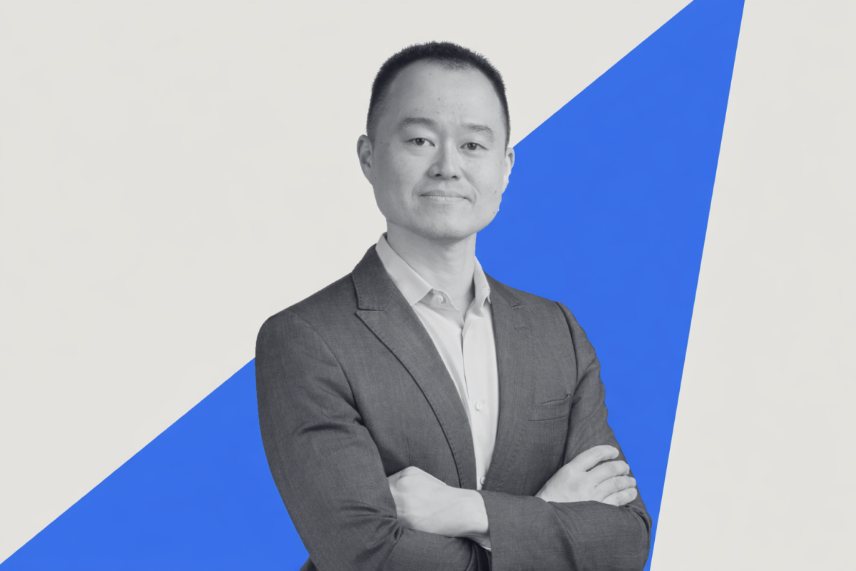 Black-and-white portrait of Jiunn Shih in a suit with his arms crossed, standing confidently against a light background with a bold blue diagonal ray cutting across the image.