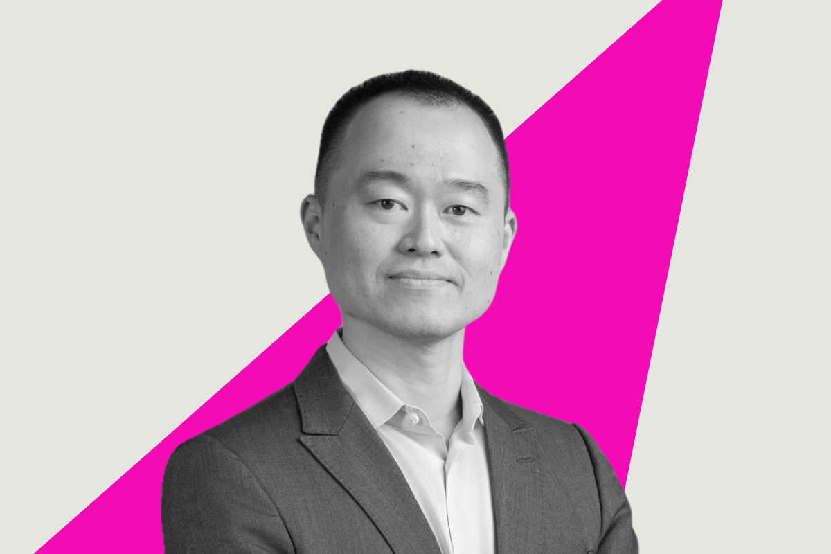 Black-and-white portrait of Jiunn Shih in a suit with his arms crossed, standing confidently against a light background with a bold pink diagonal ray cutting across the image.